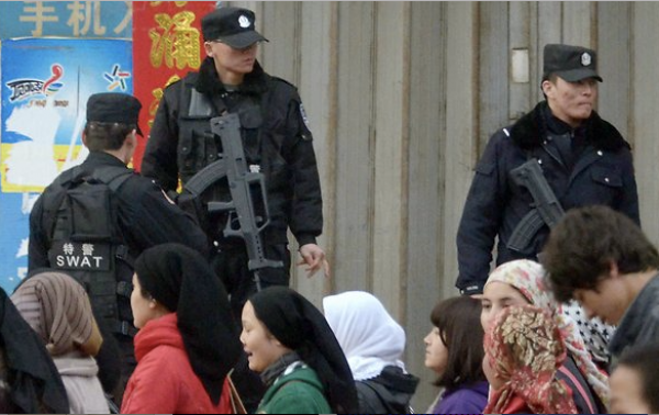在叶城，新疆人的旁边站着全副武装的警察。（AP档案图片）