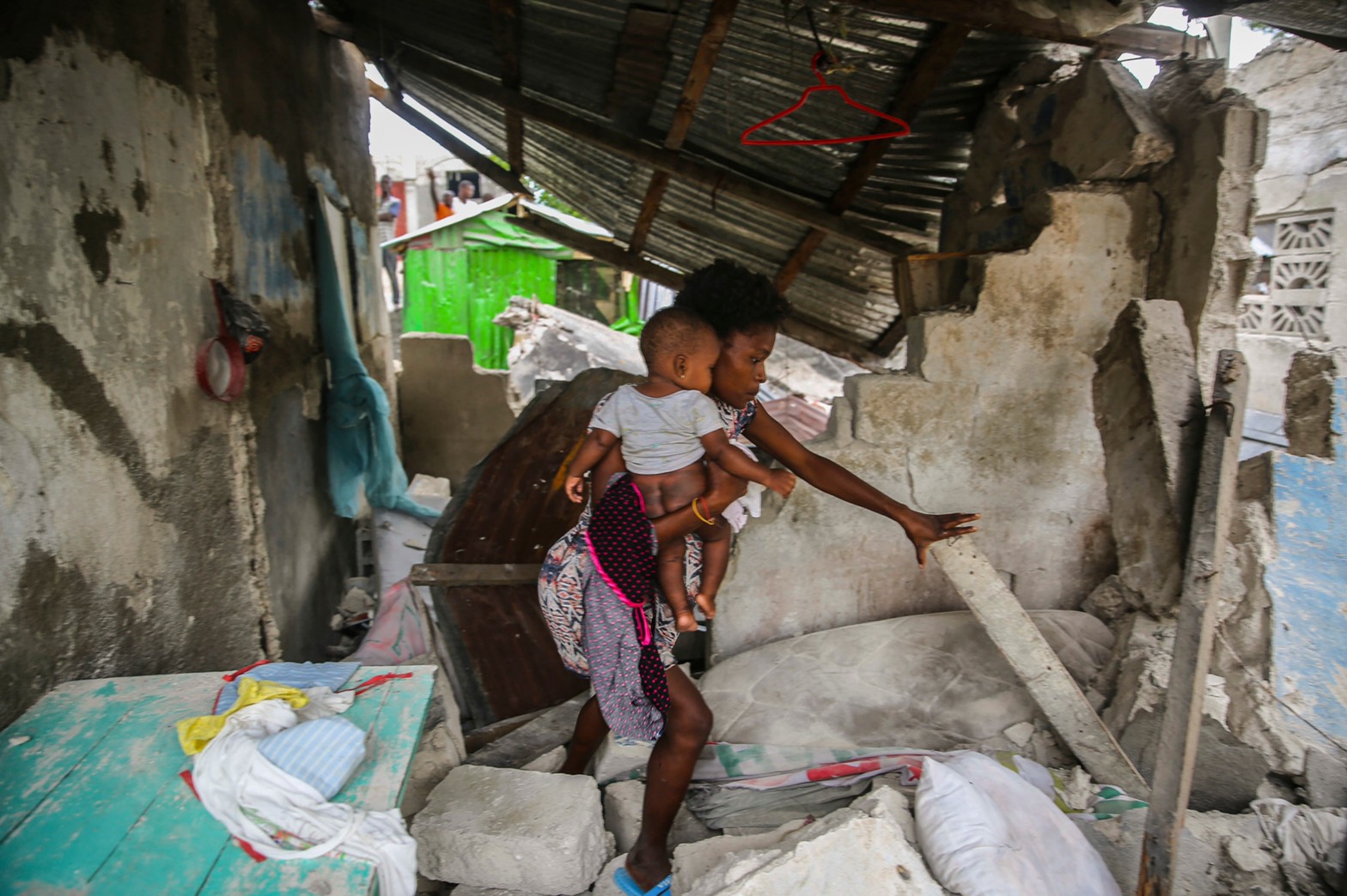 圖為2021 年 8 月 15 日星期日，一名婦女抱著她的孩子在被星期六 7.2 級地震摧毀的家中翻找財物。