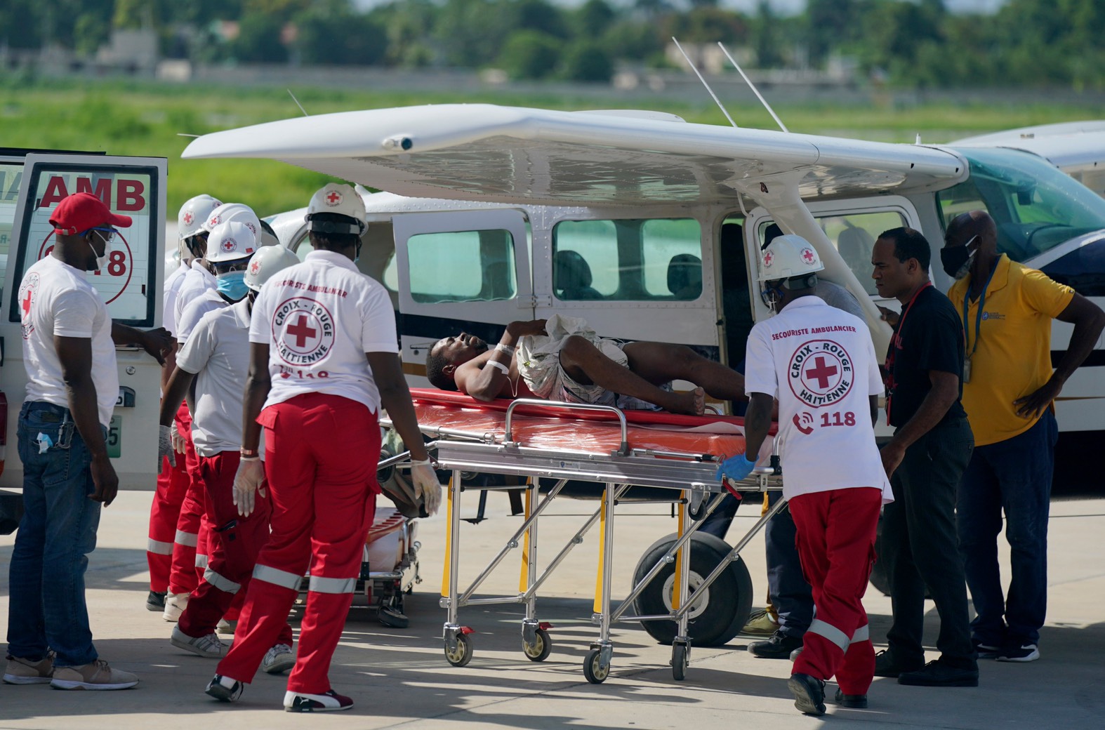 圖為2021 年 8 月 15 日星期日，在海地太子港杜桑•盧維杜爾機場當地航站樓，從 Les Cayes 市空運的地震受害者被衛生工作者轉移到救護車上。海地 7.2 級地震造成的死亡人數飆升，救援人員在即將到來的熱帶風暴可能引發洪水之前，在瓦礫中迅速尋找倖存者。 