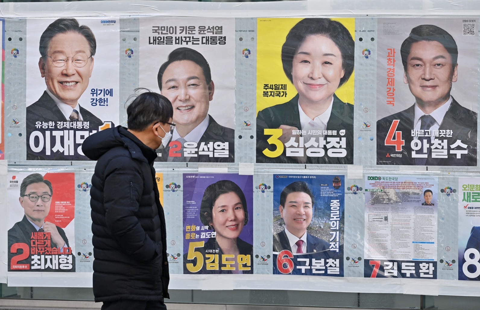 2022 年 3 月 6 日，在 3 月 9 日的總統選舉前，一名男子走過首爾的韓國總統候選人海報（上排）。