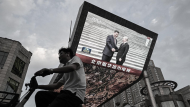普京任后首访北京 习近平罕见举行记者会。图为2024年5月16日，一名男子骑车经过一家购物中心的巨型屏幕，屏幕上正在播放关于俄罗斯总统弗拉基米尔-普京对北京进行国事访问的新闻报道。(Photo by HECTOR RETAMAL/AFP via Getty Images)